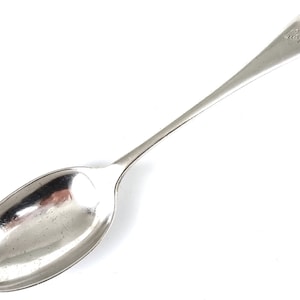 Può includere: Un cucchiaio d'argento con una ciotola arrotondata e un manico lungo e sottile. Il manico è inciso con la parola "Magdalen".