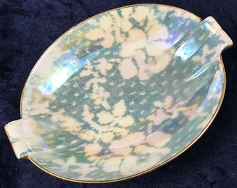 May include: A small, oval-shaped dish with a light blue and white iridescent pattern. The dish has a gold rim and two small handles on either side.