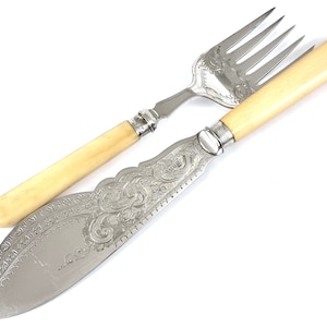 Puede incluir: Un juego de cuchillo y tenedor de mantequilla con mango de plata y marfil con un diseño ornamentado. El cuchillo tiene una hoja curva y el tenedor tiene cuatro dientes.