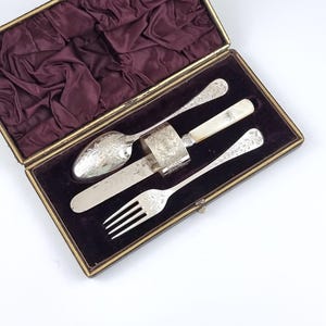 Hoja desgastada, juego de bautizo antiguo, cubiertos infantiles en caja, baño de plata, iniciales grabadas, cuchara y tenedor, dorso floral, servilletero