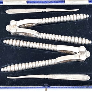 Puede incluir: Un juego de tres cascanueces de plata y un pinza para nueces en una caja forrada de terciopelo azul. Los cascanueces tienen un diseño de cuentas y la pinza para nueces tiene un diseño grabado.