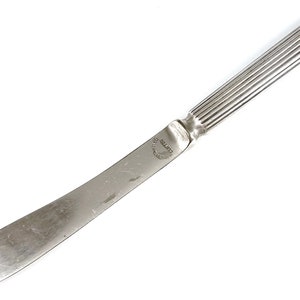 May include: A silver butter knife with a fluted handle and the word "CRUSTON" engraved on the blade.