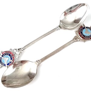 Puede incluir: Dos cucharas de plata con emblemas de la Real Fuerza Aérea Australiana esmaltados. Las cucharas tienen un diseño esmaltado azul y rojo con las palabras "Royal Air Force" y "Ad Astra" en los emblemas.