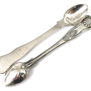May include: Two silver teaspoons with ornate handles. The spoons have a rounded bowl and a long, slender handle.