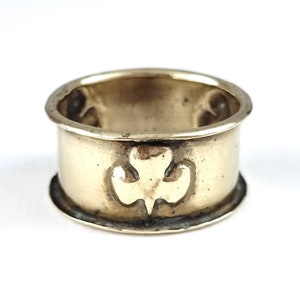 May include: A gold-colored metal napkin ring with a shamrock design.