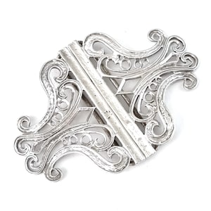 Puede incluir: Una hebilla de filigrana de plata con un diseño delicado e intrincado. La hebilla está hecha de dos piezas que se unen en el medio. El diseño presenta espirales, bucles y círculos.