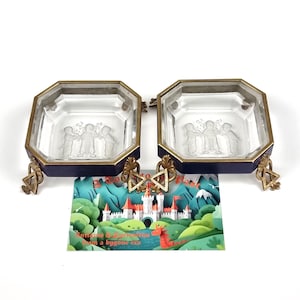 Könnte beinhalten: Zwei antike Glasschalen mit achteckiger Form, mit einem goldfarbenen Metallrahmen und dunkelblauen Akzenten. Jede Schale hat ein detailliertes geätztes Design von Figuren. Die Schalen sind durch ein dekoratives Element verbunden und ruhen auf verzierten Füßen.