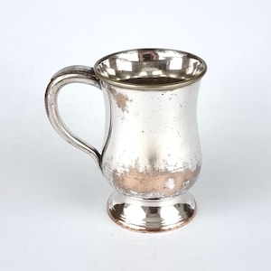 May include: A silver-plated, footed,  goblet-shaped mug with a handle. The mug has a slightly tarnished appearance.