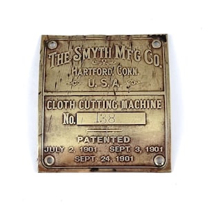 Pode incluir: Uma placa de latão com o texto "THE SMYTH MFG CO. HARTFORD, CONN. U.S.A. CLOTH CUTTING MACHINE No. 138 PATENTED JULY 2, 1901 SEPT. 3, 1901 SEPT 24, 1901"