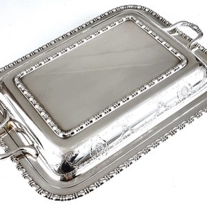 May include: Silver serving dish with a lid and two handles. The dish has a beaded edge and an engraved design.