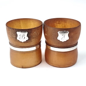 Puede incluir: Dos pequeñas tazas de madera marrón con bandas plateadas y las iniciales grabadas "B" y "J" en la parte delantera.