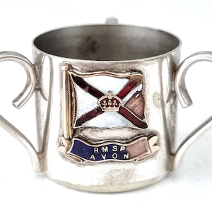 May include: Silver cup with two handles, featuring a red, white, and blue flag with a gold crown and the text "RMSP AVON" on a blue and gold ribbon.