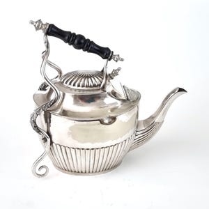 Może przedstawiać: Srebrny czajnik z czarnym drewnianym uchwytem i ozdobnymi, zakrzywionymi wspornikami. Czajnik ma żebrowany wzór na dolnej części i ozdobną pokrywę. Dzióbek jest zakrzywiony, a design jest elegancki i vintage.