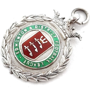 Può includere: Medaglia d'argento con un designo in smalto verde e bianco. La medaglia presenta il testo "Edmonton & District Football League" e uno scudo rosso con tre spade.