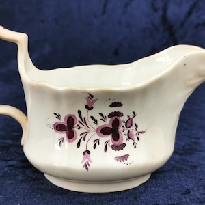 Puede incluir: Una salsera de porcelana blanca con un diseño floral rosa y marrón. La salsera tiene un asa curva y un pico.