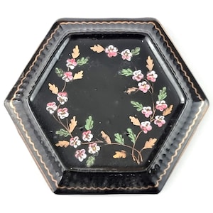 Puede incluir: Una bandeja hexagonal negra con un borde dorado y un diseño floral pintado en rosa y blanco.