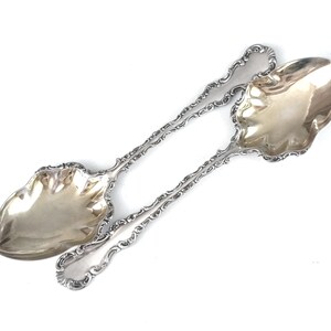 Peut inclure: Deux cuillères à sucre en argent avec des manches ornés et un bol en forme de cœur.