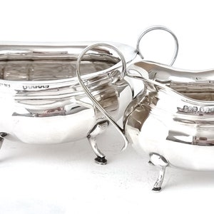 May include: A set of two silver sauce boats with ornate handles and three feet each. The boats are polished and have a reflective surface.