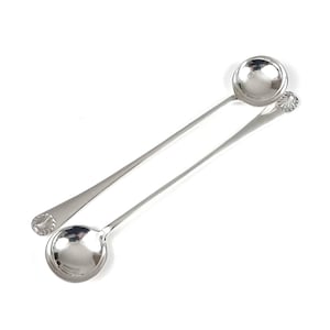 May include: Two stainless steel bar spoons with long handles and round bowls. The spoons have a polished finish, reflecting the light. The handles have a decorative shell-like design at the end. The spoons are designed for mixing cocktails.