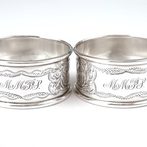 Puede incluir: Dos anillos de servilleta de plata con un diseño grabado y las iniciales "MMFS" en cada uno.