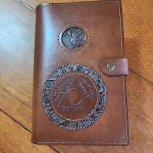 May include: Brown leather journal with a circular embossed design featuring a triangle with the words "To thine own self be true", "Unity", "Service", and "Recovery".
