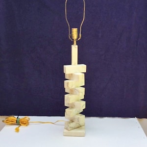 May include: A white marble table lamp with a stacked geometric design. The lamp has a gold metal base and a white fabric shade.