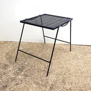 May include: A black metal side table with a square wire mesh top. The table has a simple, modern design and is perfect for a small space.