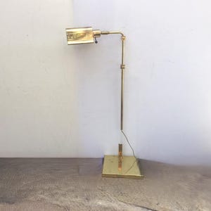 May include: A brass floor lamp with a rectangular shade and a long, adjustable arm. The lamp has a simple, modern design.