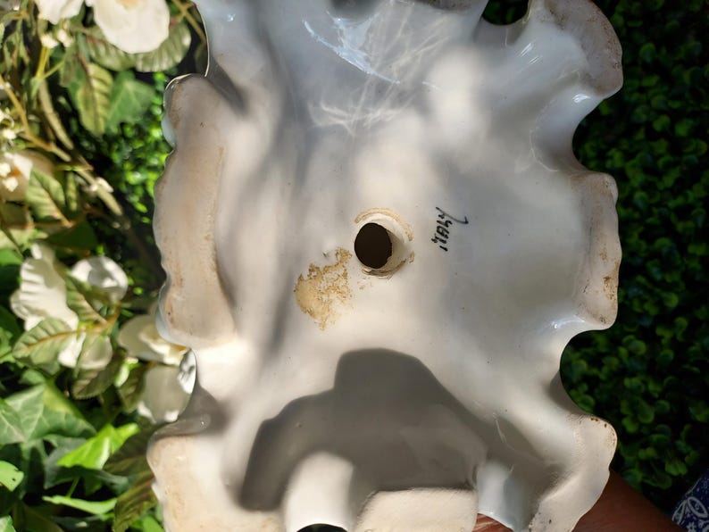 May include: White ceramic figurine with a ruffled edge and a hole in the center. The bottom of the figurine is marked "Italy".