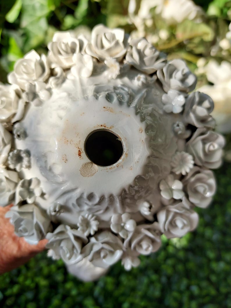 May include: White ceramic vase with a floral design. The vase is decorated with raised roses and other flowers. The vase has a hole in the bottom for drainage.