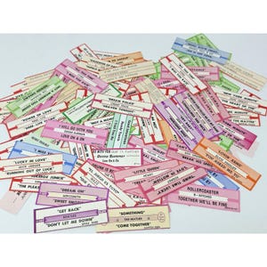 May include: A collection of colorful vintage music ticket stubs with song titles and artist names. The stubs are in various colors, including pink, green, and purple, and feature text like "Dream On" and "Come Together."