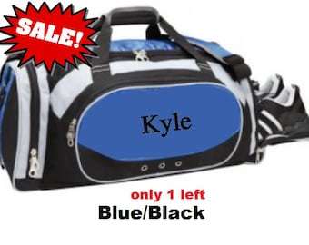 May include: Blue and black duffel bag with a blue oval panel featuring the name "Kyle" in black. The bag has white accents, a top handle, and a shoulder strap. A pair of black and white sneakers is visible on the side. The text "SALE!" is in a red burst.