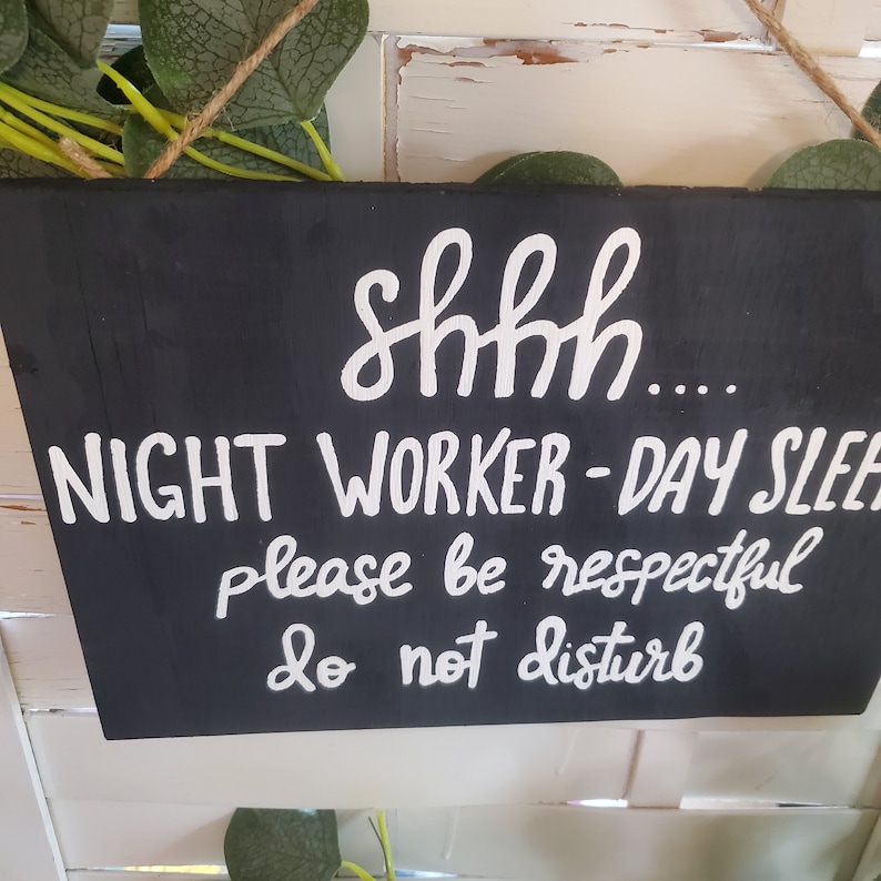 May include: Black sign with white text that reads "Shhh... Night Worker - Day Sleeper. Please be respectful. Do not disturb."