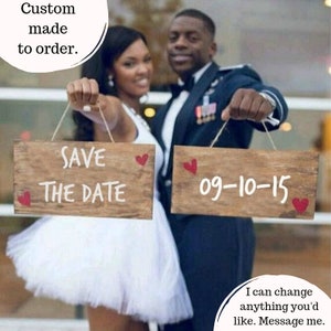 May include: A couple holding two wooden signs with the text "Save the Date" and "09-10-15". The signs are decorated with red hearts. The text "Custom made to order. I can change anything you'd like. Message me." is also visible.