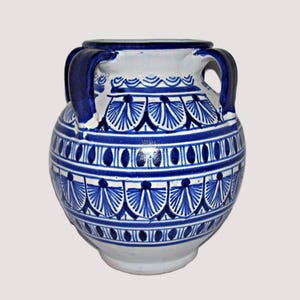 May include: A blue and white ceramic vase with two handles. The vase features a repeating pattern of blue fan-like shapes and oval designs. The top and base are white, and the handles are a darker blue.