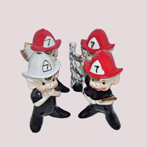May include: Set of four ceramic figurines of elves dressed as firefighters. Each elf is wearing a red and white firefighter hat with the number 7 on it. The elves are wearing black pants and have white faces with painted features. One elf is holding a ladder.
