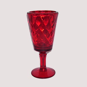 May include: A ruby red glass goblet with a diamond pattern on the bowl. The stem and base are also red. The glass is transparent, allowing light to pass through. The goblet is likely used for serving beverages.