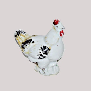 May include: A ceramic hen figurine, predominantly white with black and yellow markings on the tail and wings. The hen has a red comb and wattle. The figurine is a decorative item.