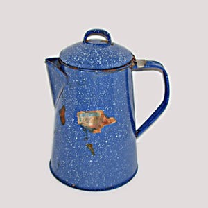 May include: Vintage blue enamelware coffee pot with white speckles. Features a lid with a handle, a spout, and a curved handle. The pot has some rust spots and a faded sticker.