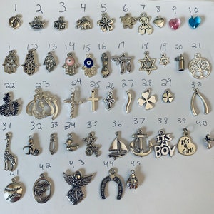 May include: A collection of 45 silver charm pendants, including a variety of religious, animal, and symbolic designs. The charms are arranged in rows on a white background.