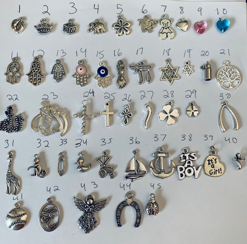 May include: A collection of 45 silver charm pendants, including a variety of religious, animal, and symbolic designs. The charms are arranged in rows on a white background.