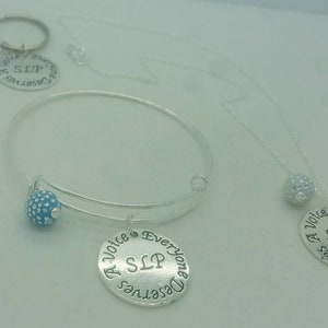 May include: Two silver necklaces with a charm that says "A Voice Everyone Deserves SLP". One necklace has a blue charm and the other has a silver charm.