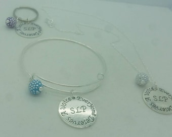 May include: Two silver necklaces with a charm that says "A Voice Everyone Deserves SLP". One necklace has a blue charm and the other has a silver charm.