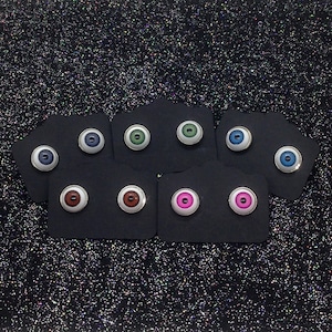 May include: Assortment of 10 eye-shaped earrings with different colored irises. The earrings are displayed on black card stock.