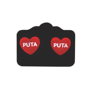 May include: Two red heart-shaped earrings with the word "PUTA" written in white on each.