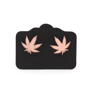 Puede incluir: Un par de pendientes de oro rosa con forma de hojas de marihuana en una tarjeta de exhibición negra.
