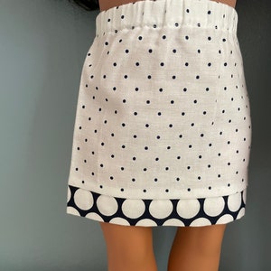 May include: A white skirt with black polka dots and a black and white polka dot trim. The skirt is made of a soft, lightweight fabric.
