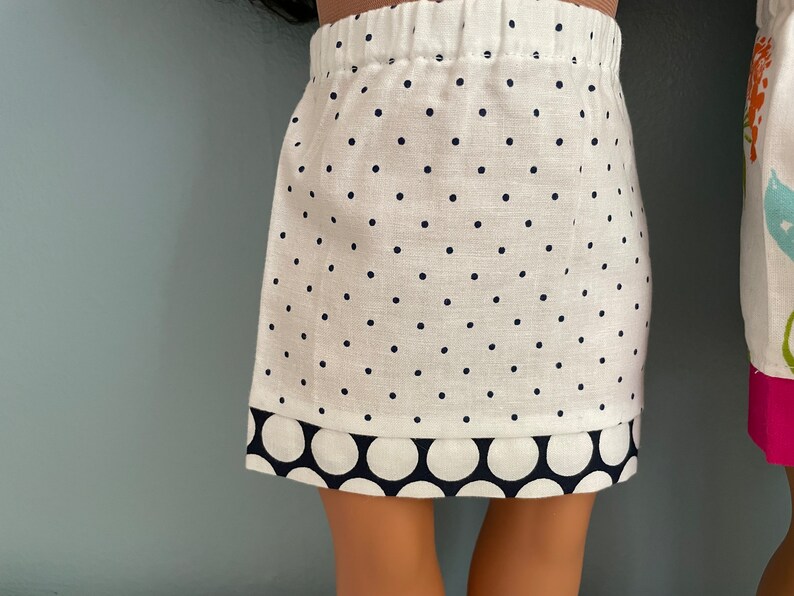 May include: A white skirt with black polka dots and a black and white polka dot trim. The skirt is made of a soft, lightweight fabric.