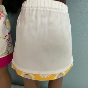May include: Two white skirts with different colored trims. One skirt has a pink trim and the other has a yellow trim with a floral pattern.