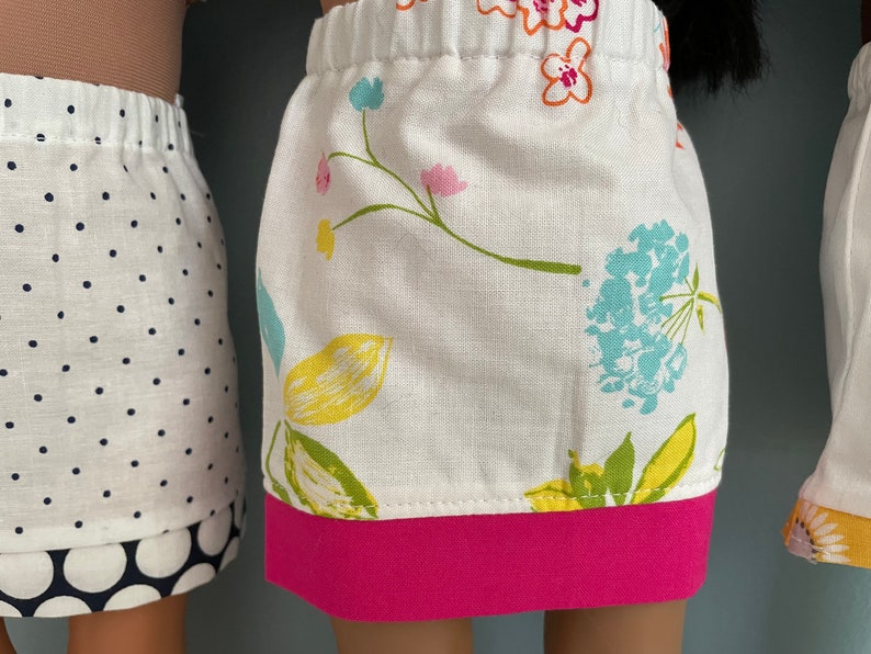 May include: Three doll skirts, one with white polka dots, one with a floral print and a pink band, and one with a yellow and orange floral print.